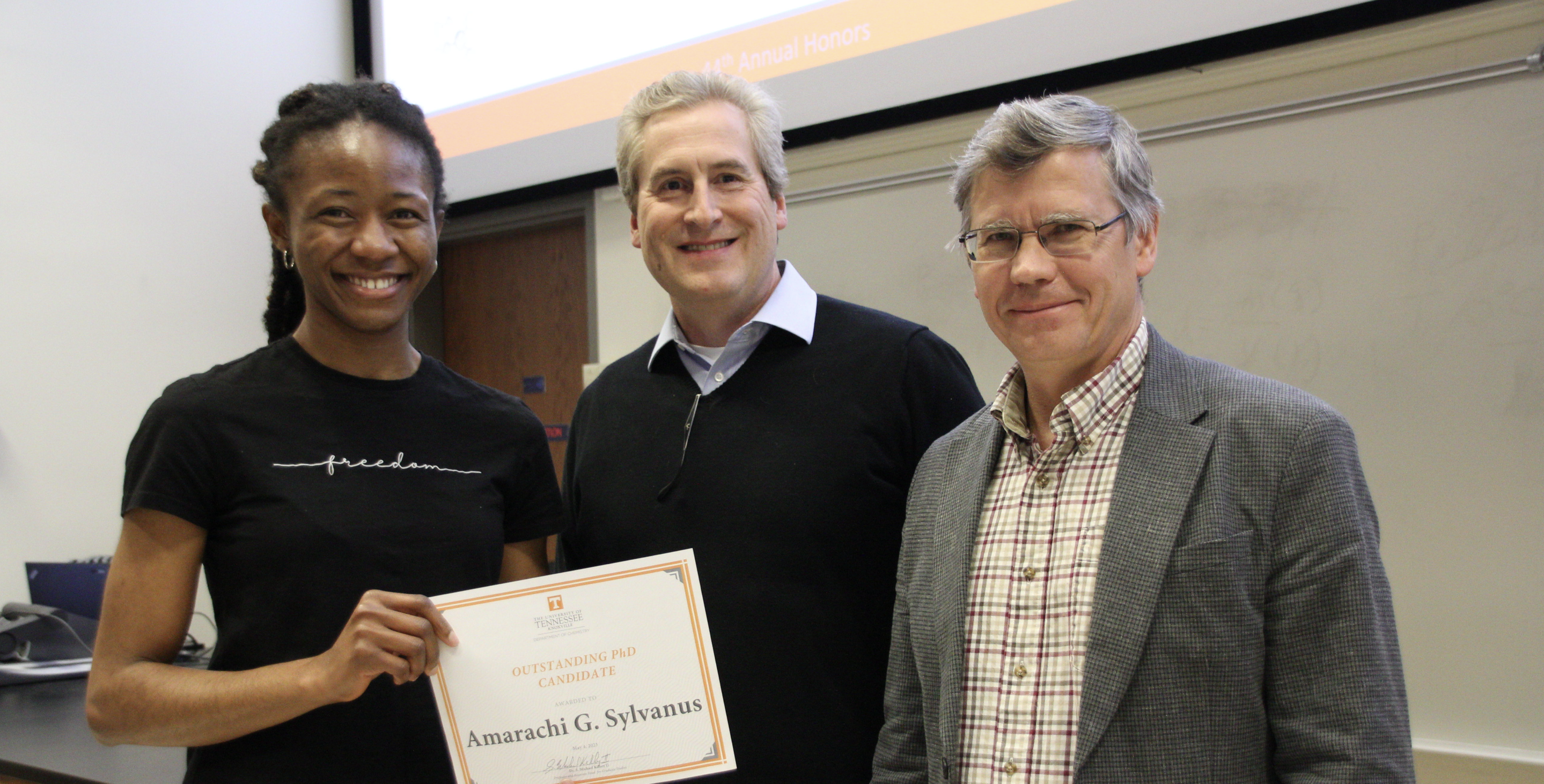 Amarachi Sylvanus poses for a photo with two men, holding a certificate for the Outstanding PhD Candidate award
